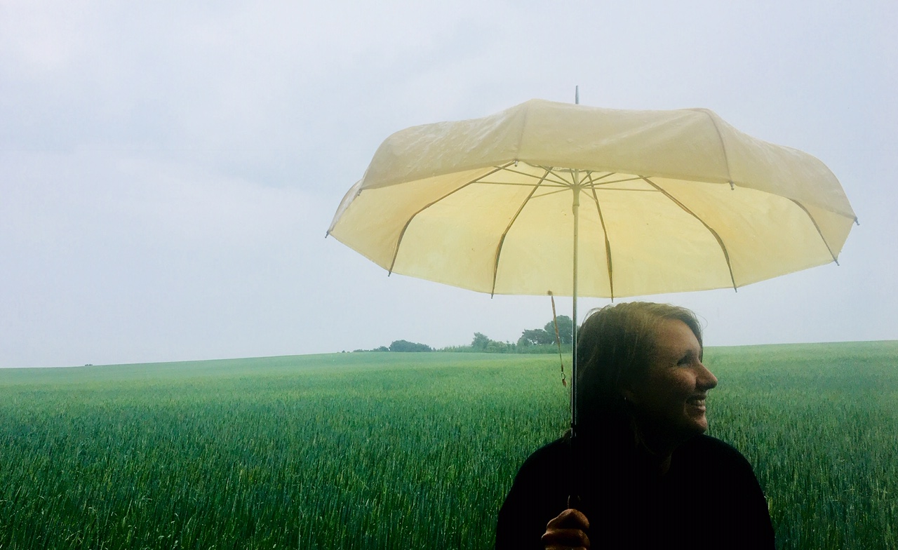 Anja Dalby i regnen med en gul paraply. Verden er venlig.